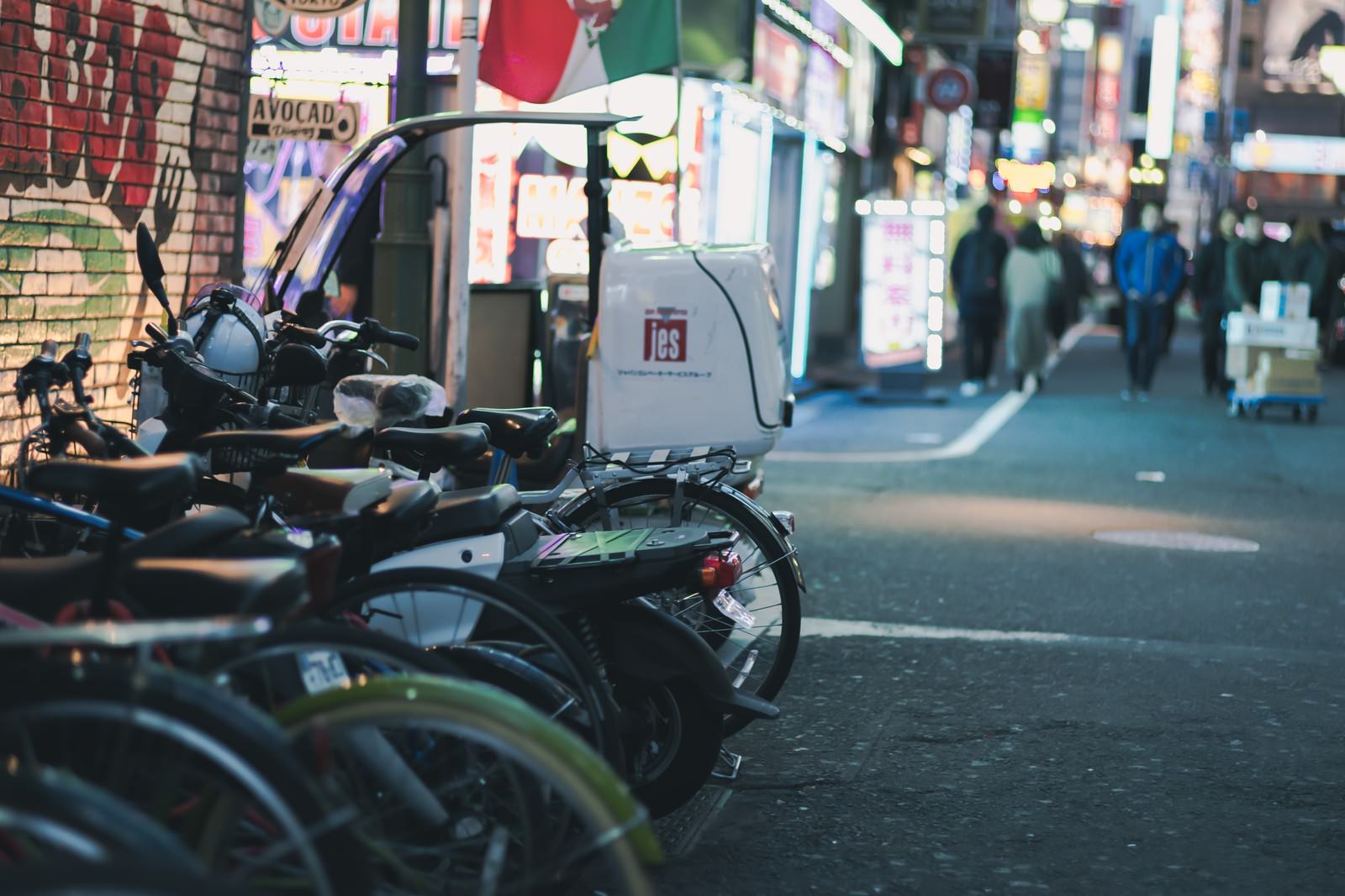 夜の路地に駐車した複数のバイクと奥に見える繁華街の明るい灯り