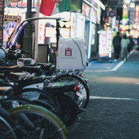 路地に駐車した複数の二輪と奥に広がる繁華街の灯りの写真