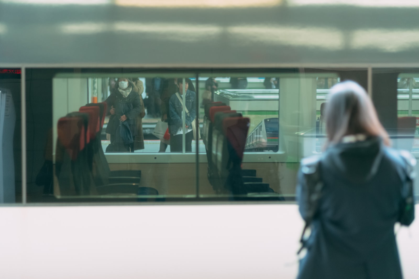 電車の車窓越しにホームで電車を待つ利用客の後ろ姿
