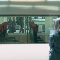 停車中の電車越しに見るホームで電車を待つ利用客の写真