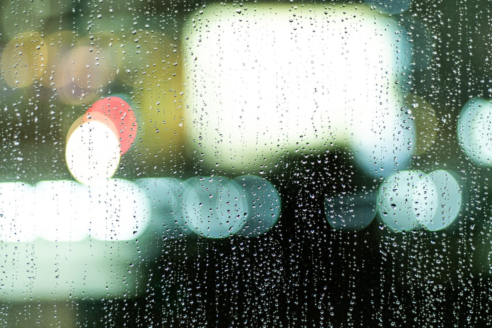 雨粒が付いた窓ガラス越しに見えるネオンの玉ボケが煌めいている
