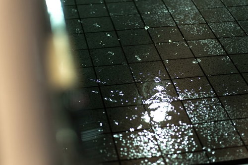 雨降りの水溜りに映る光と水滴、濡れたタイル表面の反射