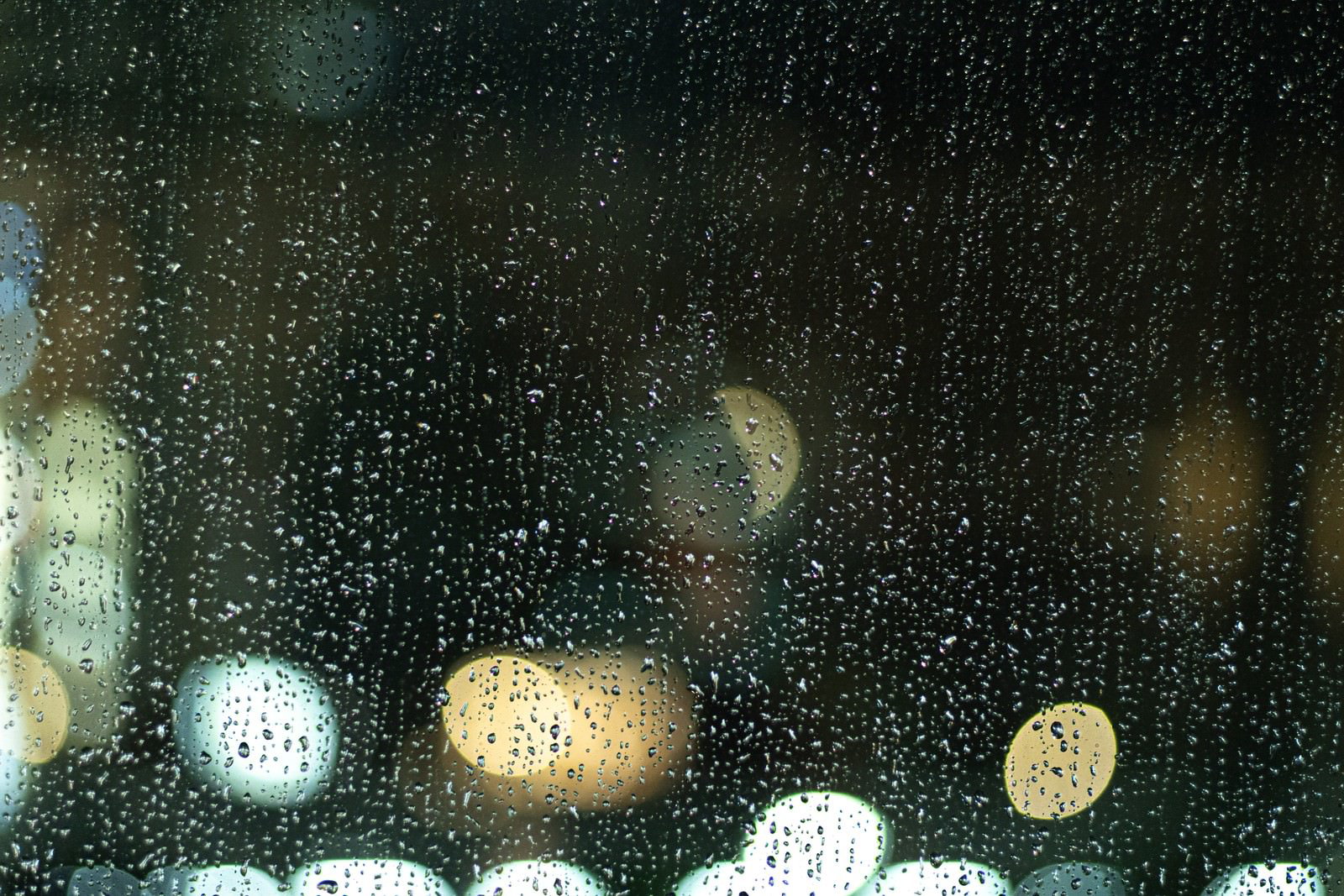 窓ガラスに付いた無数の雨粒と背景にぼけた街の夜景