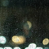 窓ガラス一面に残る雨粒と街の明かりの写真