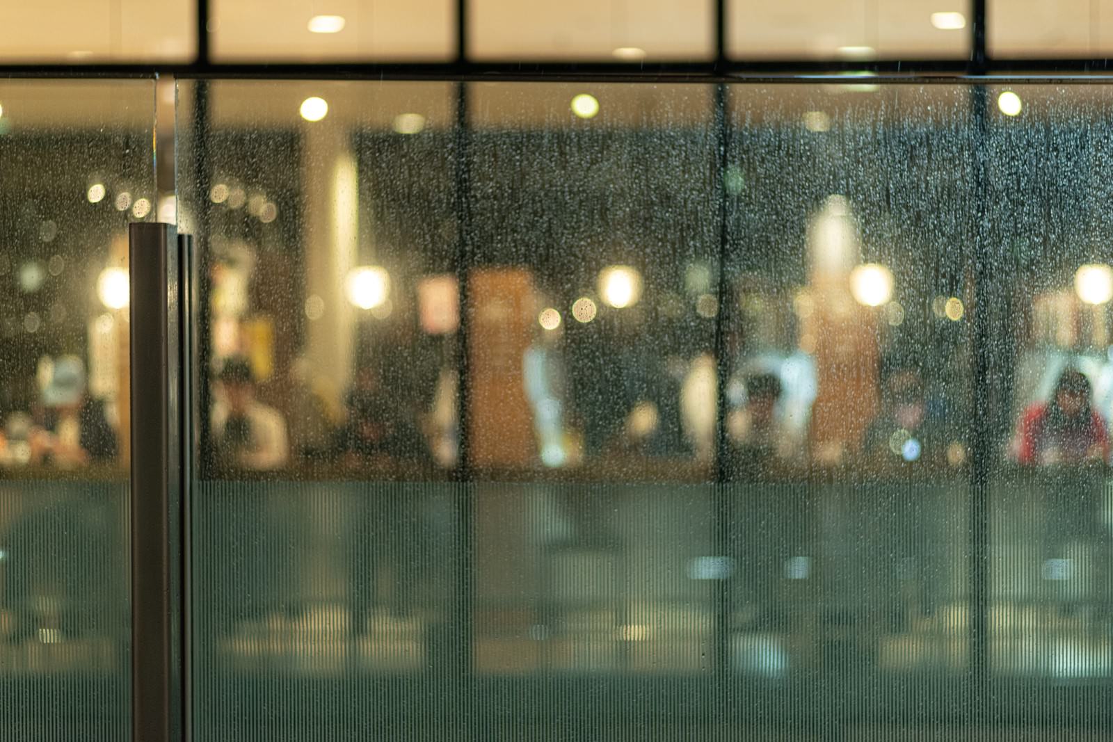 雨粒が付いたガラス越しに見えるカフェの温かい照明がボケている様子