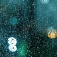ガラス窓いっぱいに付着した雨粒と光の反射の写真