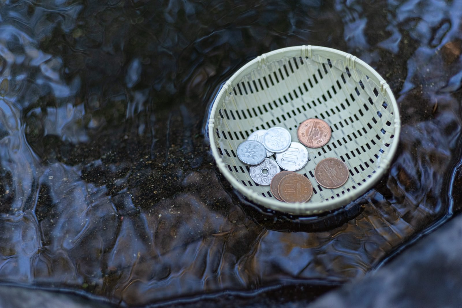 竹製のザルに入った硬貨が水の上に浮かんでいる様子