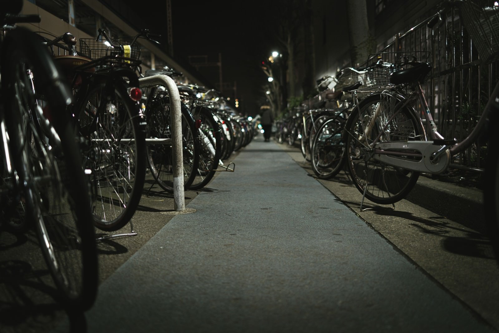 薄暗い照明の下、コンクリートの通路に自転車が並ぶ夜間の駐輪場