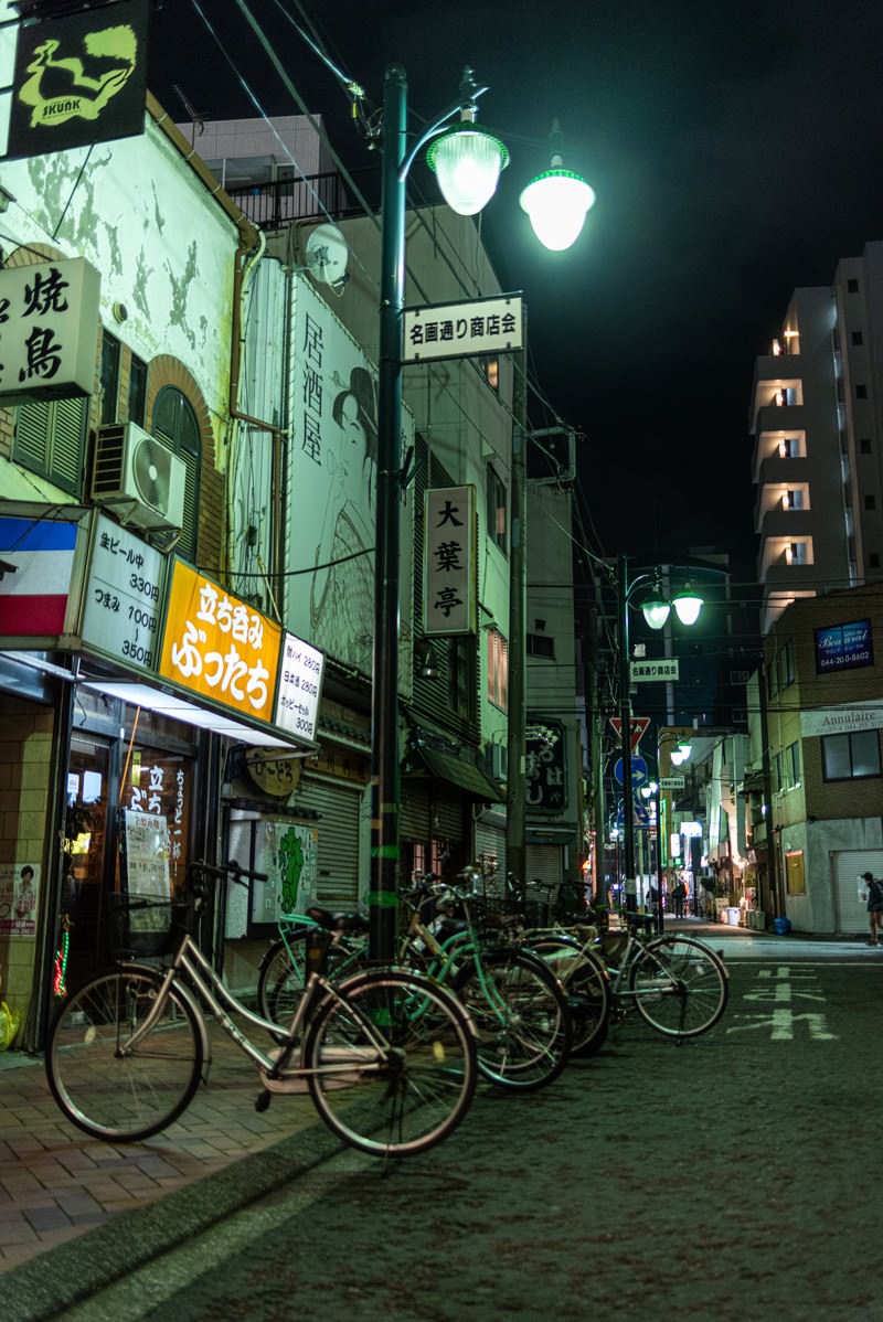 夜の名画通りの路地裏に駐輪された複数の自転車と街灯、店舗看板