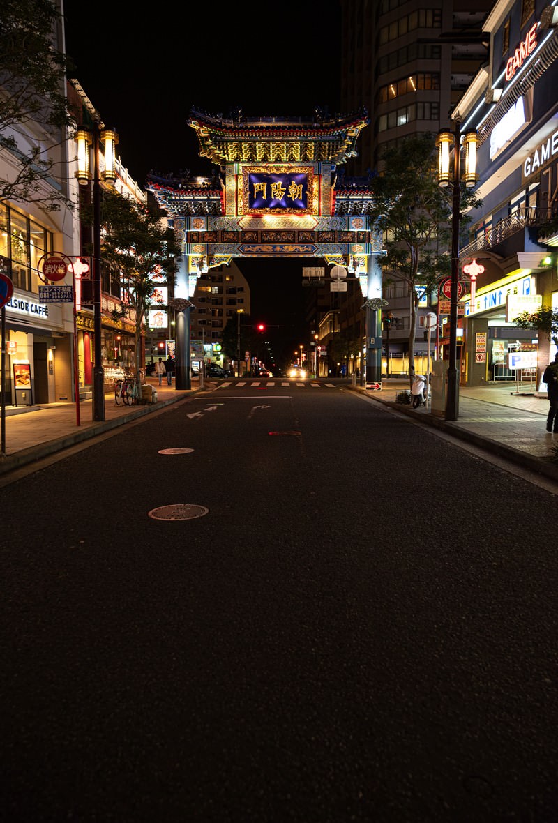 夜の横浜中華街で朱色にライトアップされた朝陽門と両側の店舗