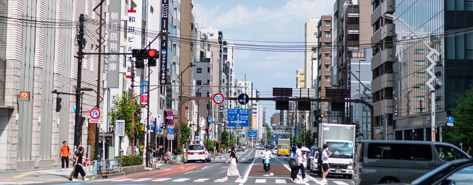 横断歩道を渡る歩行者と両側に建物が立ち並ぶ都市の街並み
