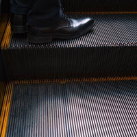 エスカレーターに乗るビジネスマンの黒い革靴と足元の写真