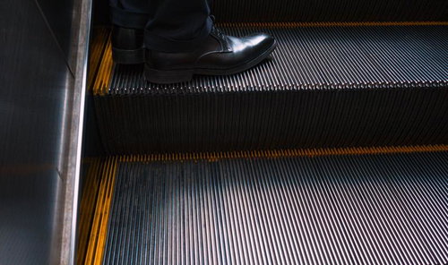 エスカレーターに乗るビジネスマンの黒い革靴と足元