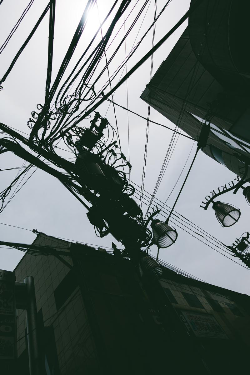 下町の電柱に複数の電線が絡み合い、シルエットで映る写真