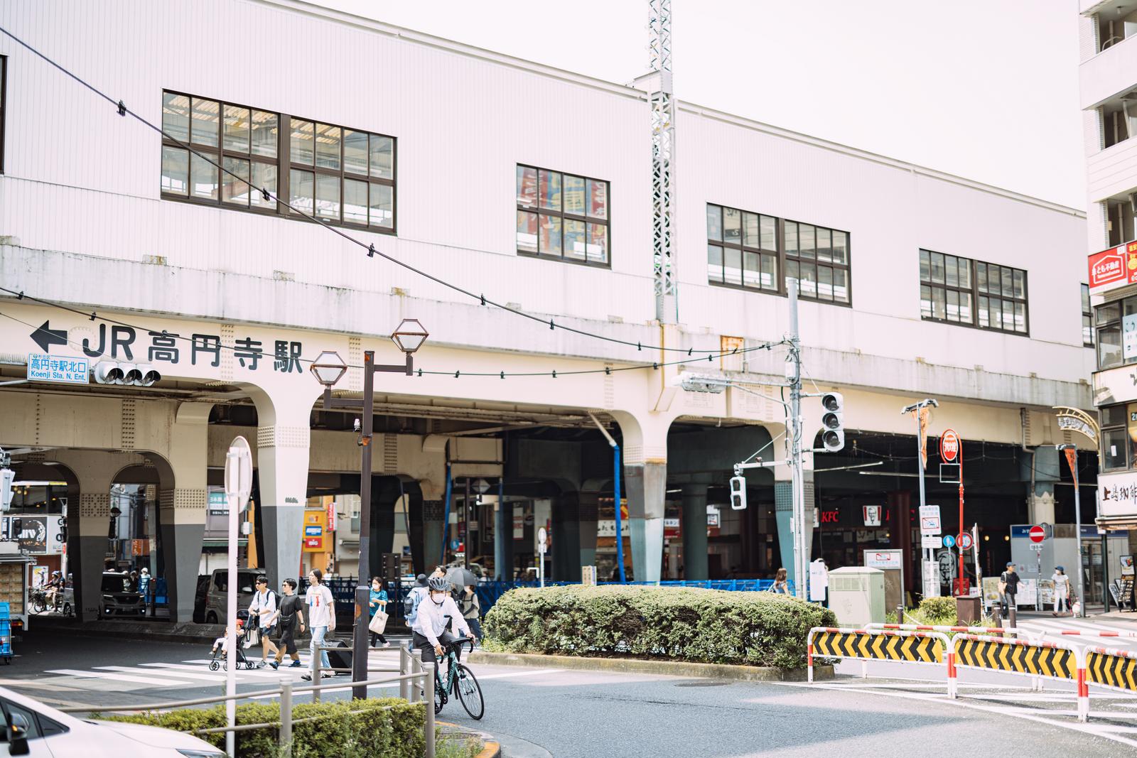 JR高円寺駅舎の前で人が行き交い自転車に乗った男性がいる駅前広場