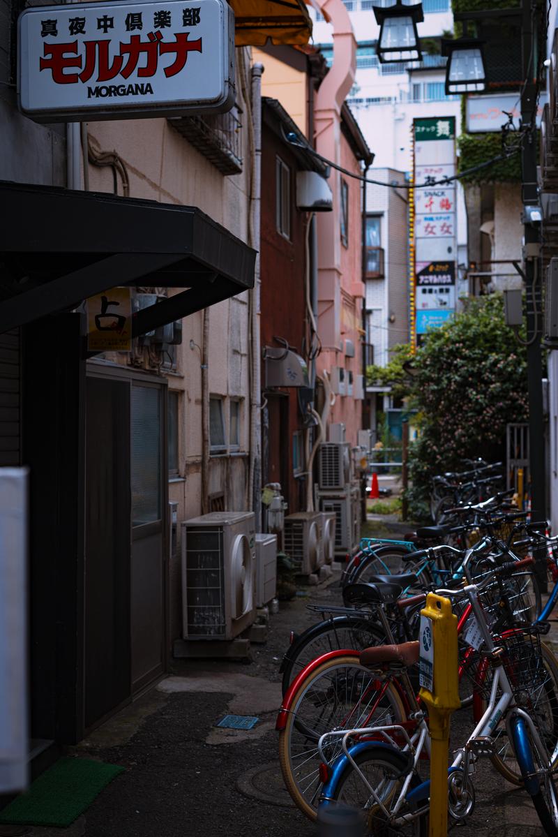 路地裏の飲み屋街に駐輪された赤と青の自転車と看板
