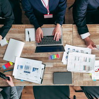 紙の資料とパソコンを用いてディスカッションする会議の写真