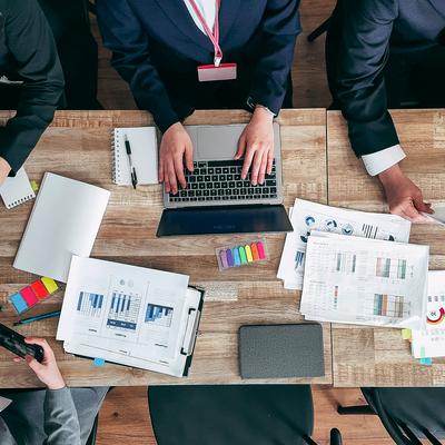 紙の資料とパソコンを用いてディスカッションする会議の写真