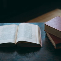 木製テーブルに広げられた洋書と積み重ねられた古書の読書の時間の写真