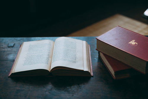 木製テーブルに広げられた洋書と積み重ねられた古書の読書の時間