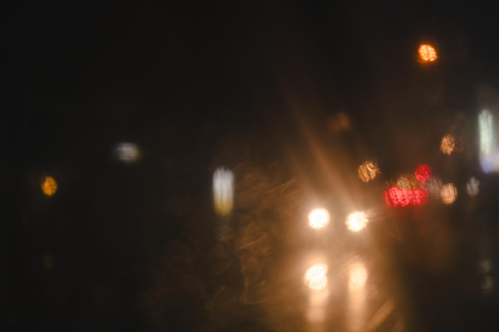 傘の水滴越しに見える夜間の対向車のヘッドライト