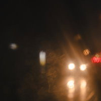 夜間の雨の中、傘越しに見える対向車のヘッドライトの写真