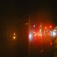 傘越しに見るテールランプと赤信号、雨の夜道の風景の写真