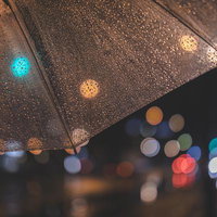 傘越しに見える雨の夜の玉ボケ。透明な傘と街灯の光の写真