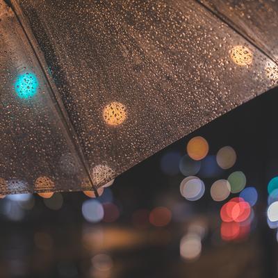 傘越しに見える雨の夜の玉ボケ。透明な傘と街灯の光の写真
