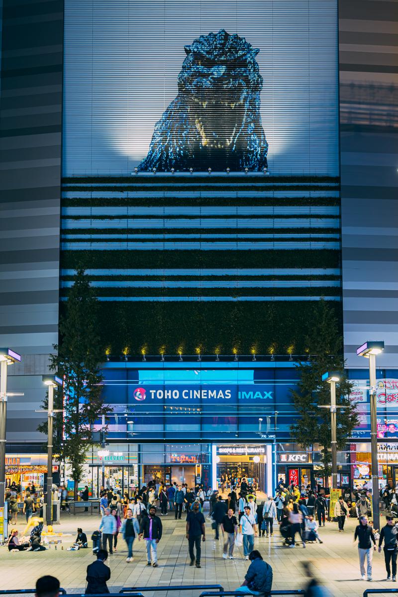 新宿歌舞伎町の夜間シネシティ広場でゴジラの映像が映るビル背景に群衆が行き交う