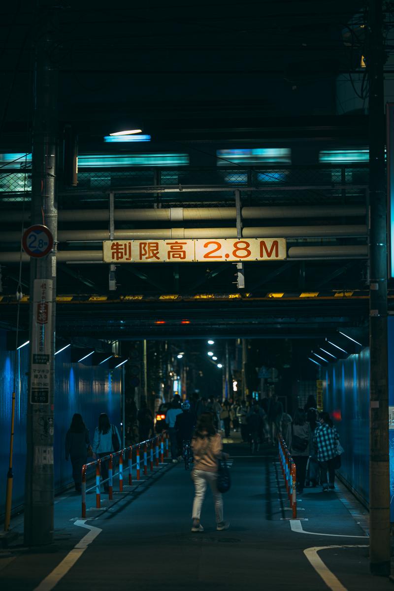夜間の駅の架線下に掲げられた黄色い制限高2.8Mの標識と人通りのある通路