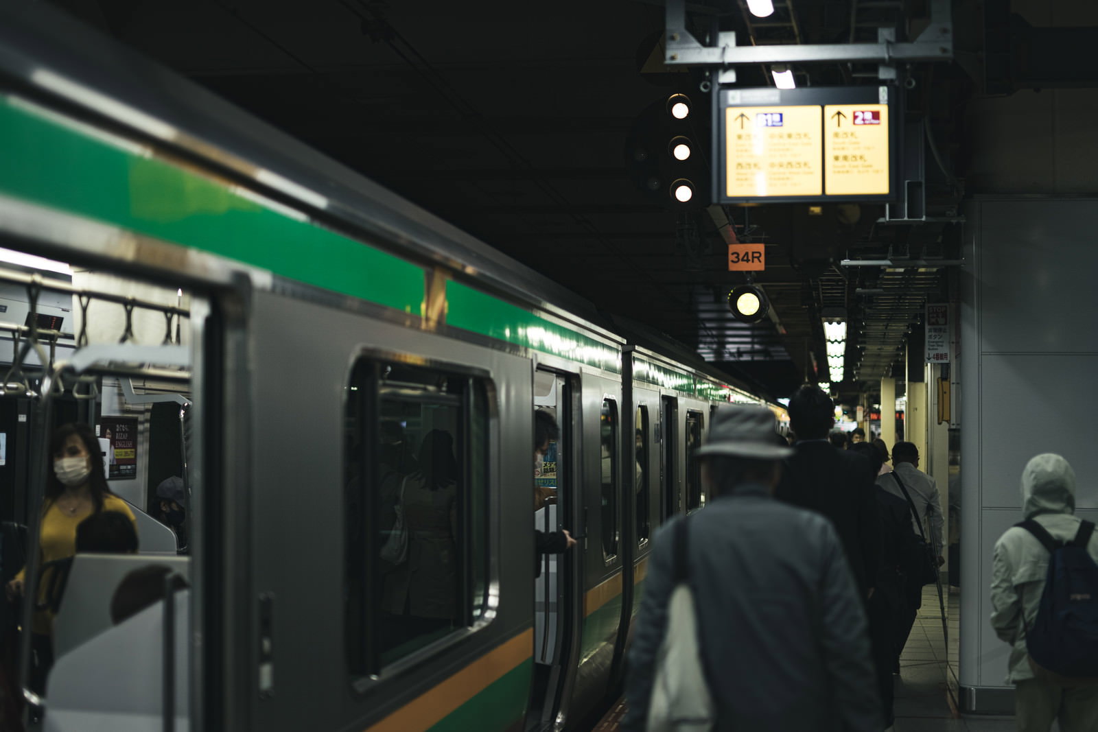 夜の駅のホームに停車する緑色の電車と乗降する乗客