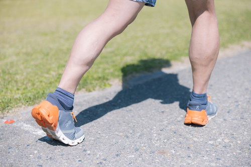 オレンジ色のランニングシューズを履いてアキレス腱を伸ばす男性の足元