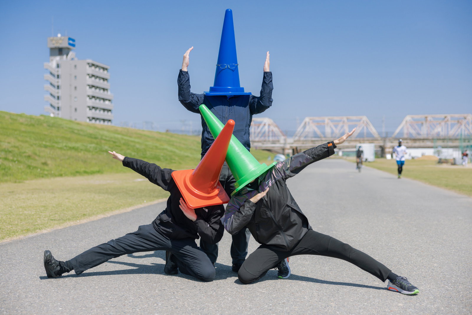 河川敷でカラーコーンをかぶって手を広げポーズを取る人たち