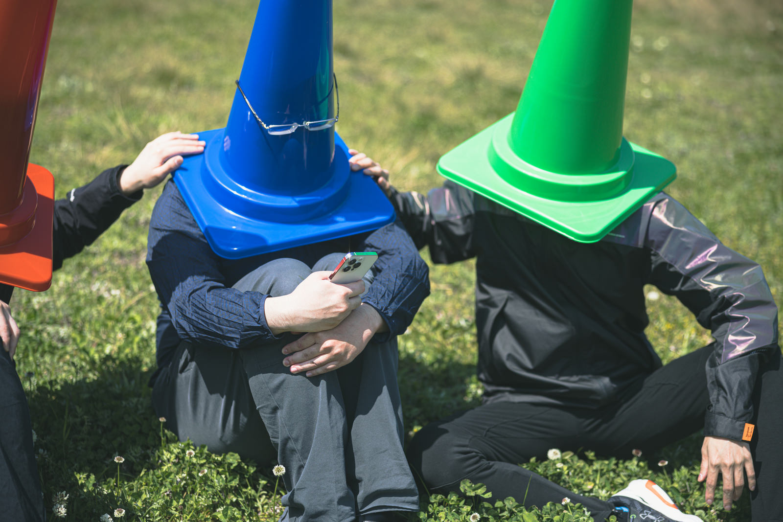 芝生の上で体育座りをする青と緑の三角コーン