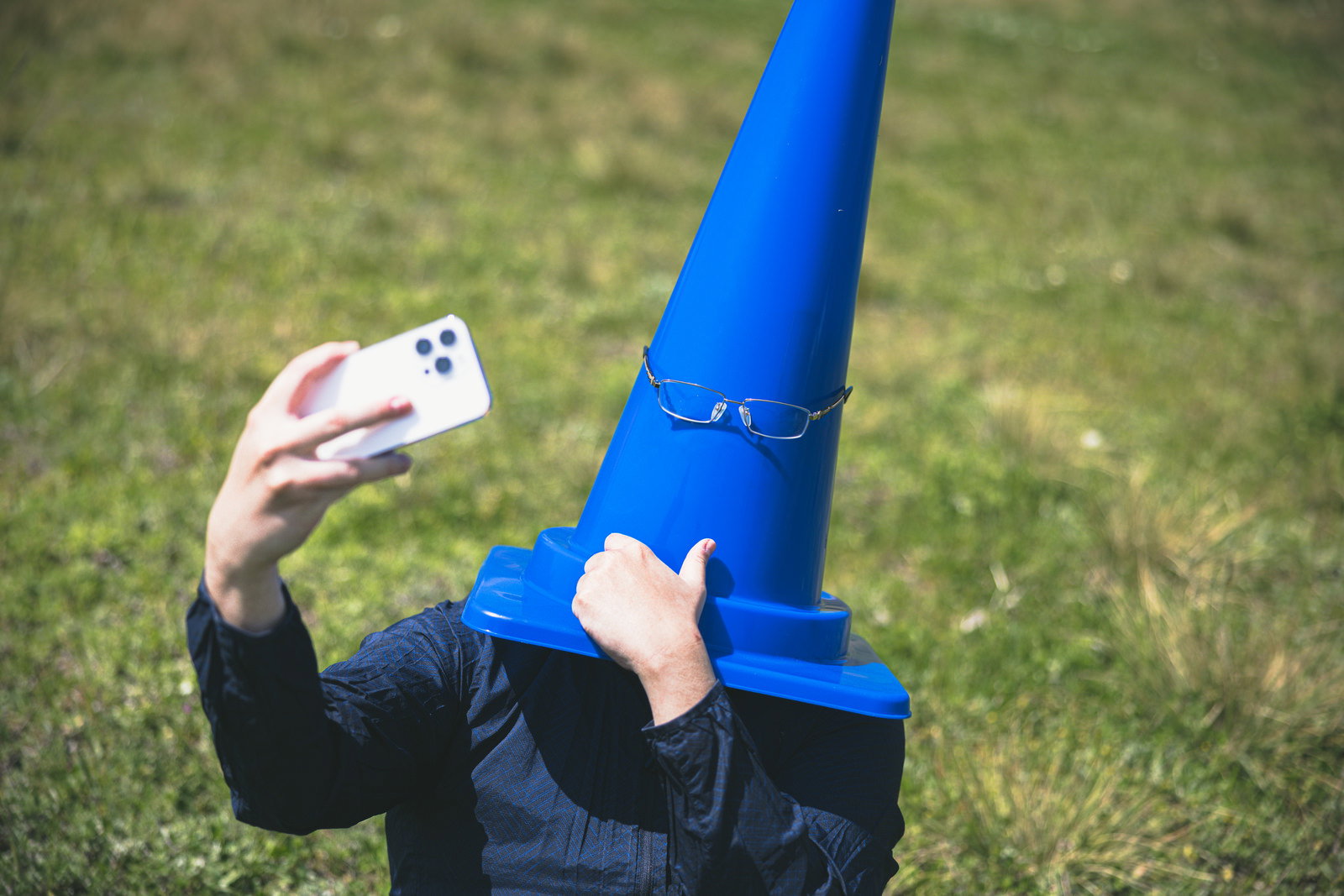 青い三角コーンが芝生の上でスマートフォンを使って自撮りをしている