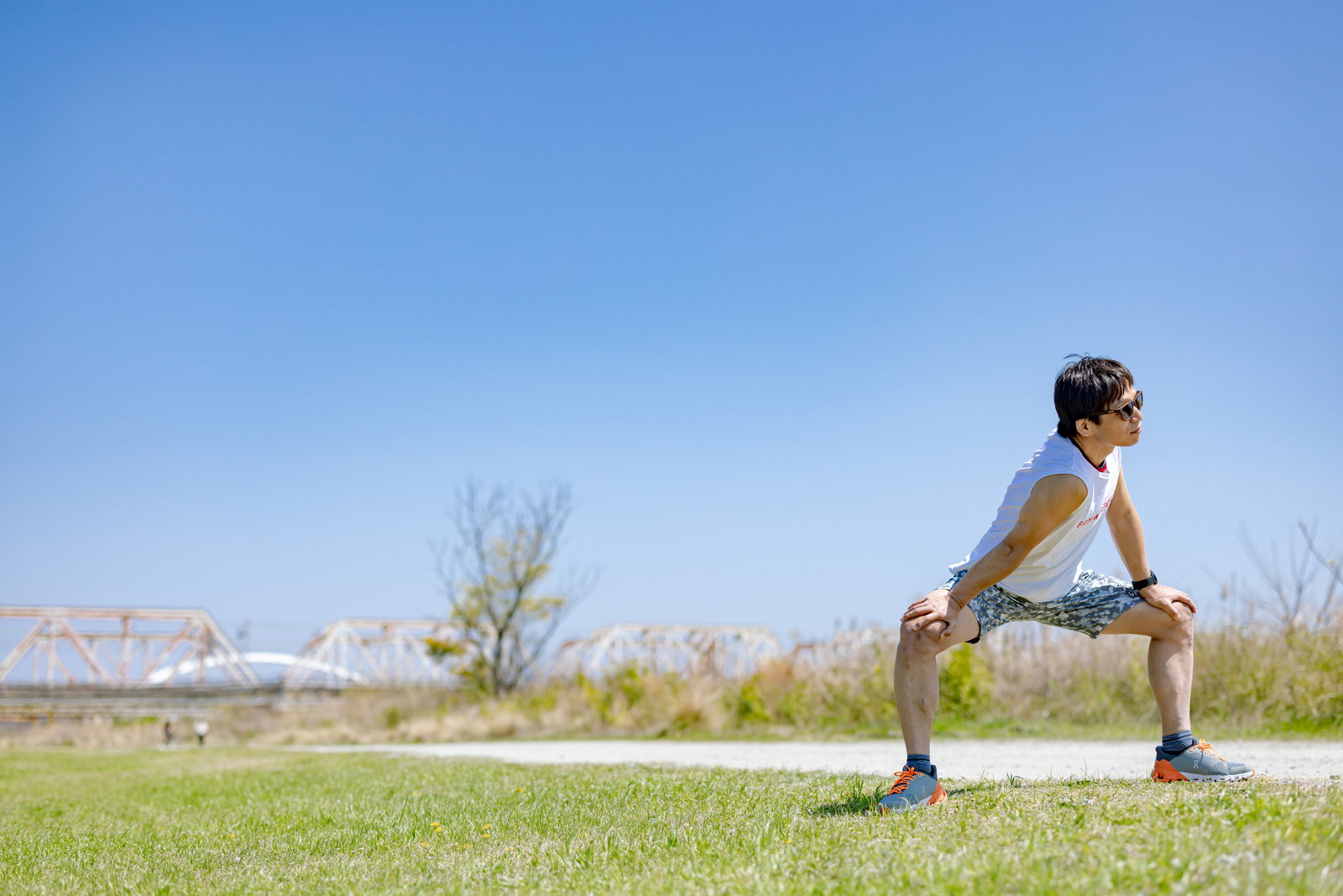 青空の下、河川敷でトレーニング準備をするトライアスロン選手の足元［モデル：うえせい］