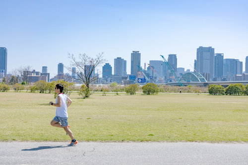 青空の河川敷をランニング中の男性、トレーニングに励む姿