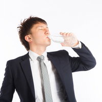 この水素水うめぇええ、スーツ姿で水分補給する営業男性の写真
