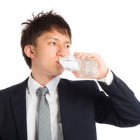 水を飲んで喉を潤すビジネスマン、スーツ姿で水分補給の写真