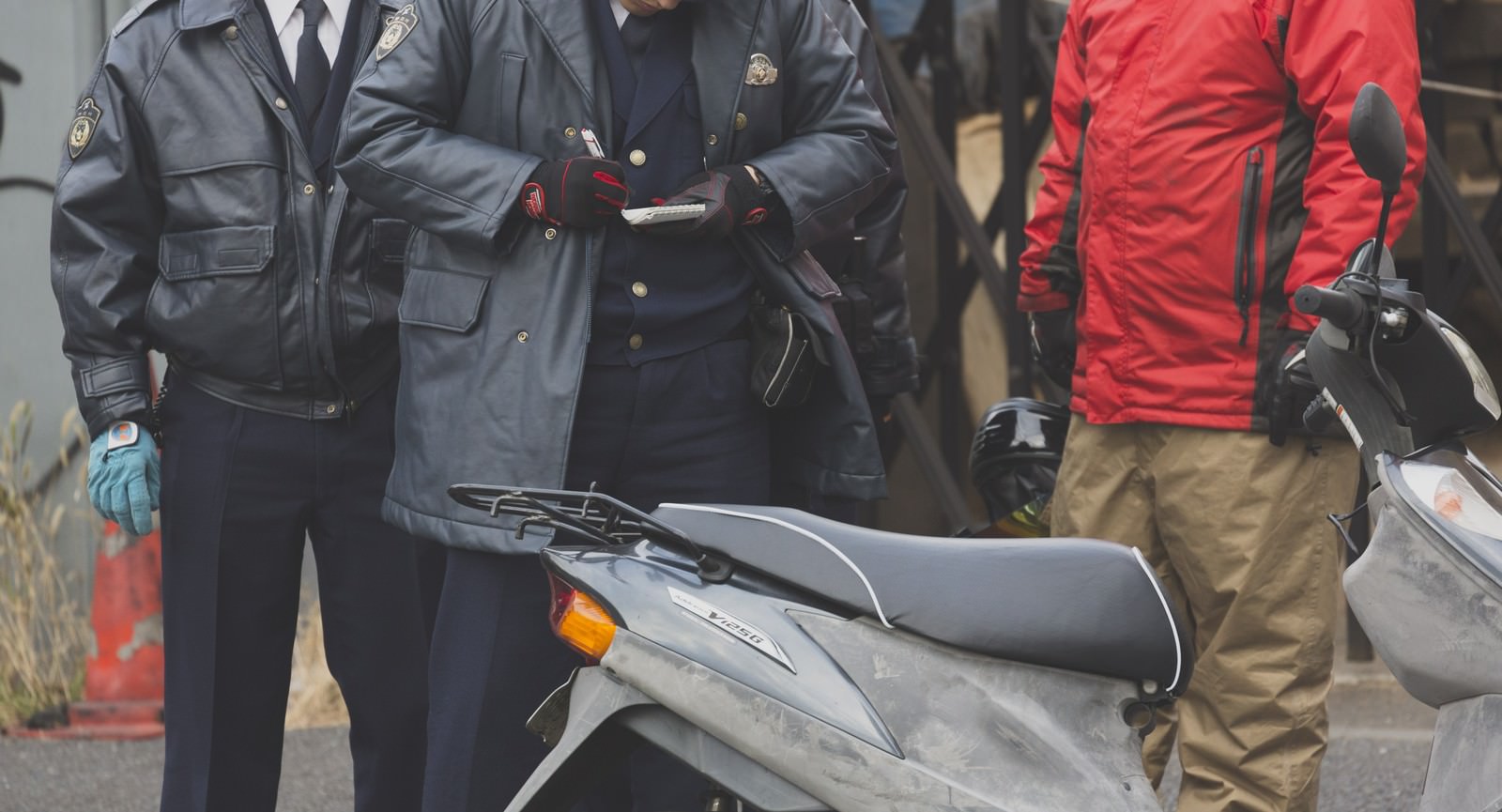 警察官が赤いジャケットの人物にバイクについて職務質問する場面