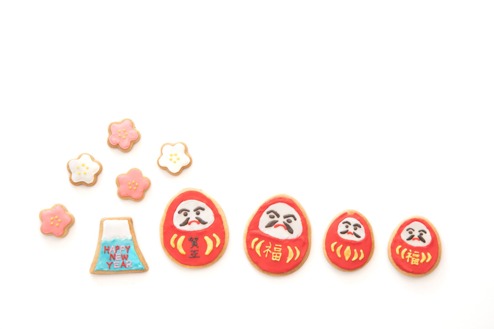 お正月のだるまとアイシングクッキーが白い背景に並んでいる様子
