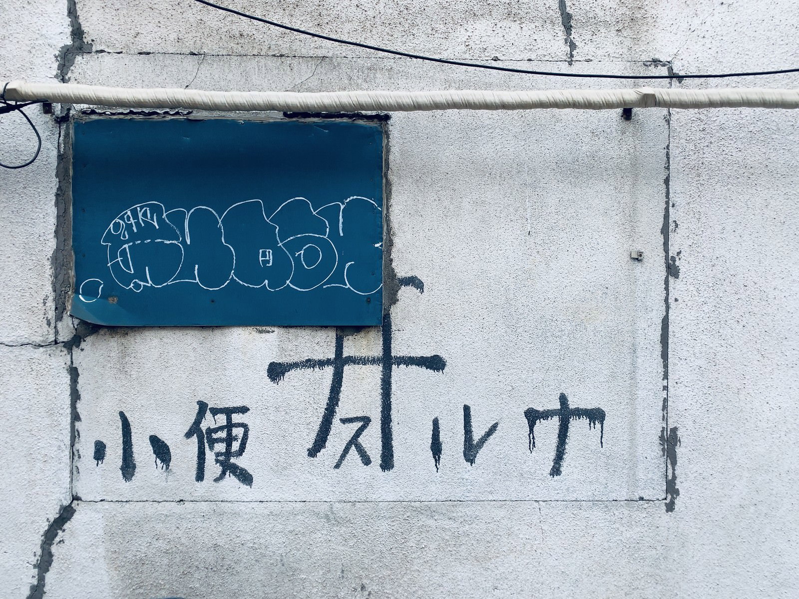 コンクリート壁に青い枠で囲まれた「小便スルナ」の文字