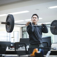 無人のオフィスでバーベルを肩に担いで挙げる社長の写真