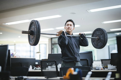 無人のオフィスでバーベルを肩に担いで挙げる社長