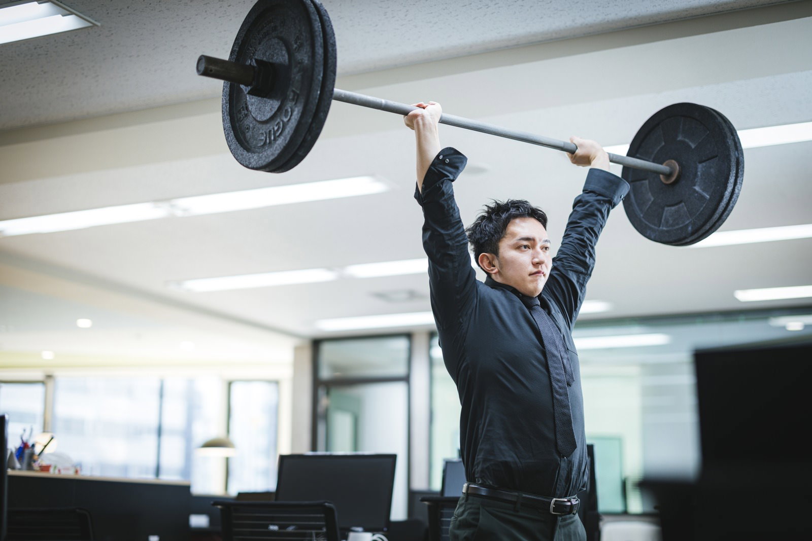 オフィスでバーベルを持ち上げている男性［モデル：鈴木秀］