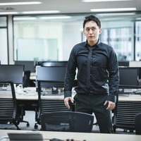 オフィスに現れた筋肉質の社長がデスク前に堂々と立つポートレートの写真