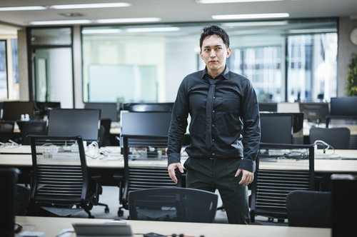 オフィスに現れた筋肉質の社長がデスク前に堂々と立つポートレート