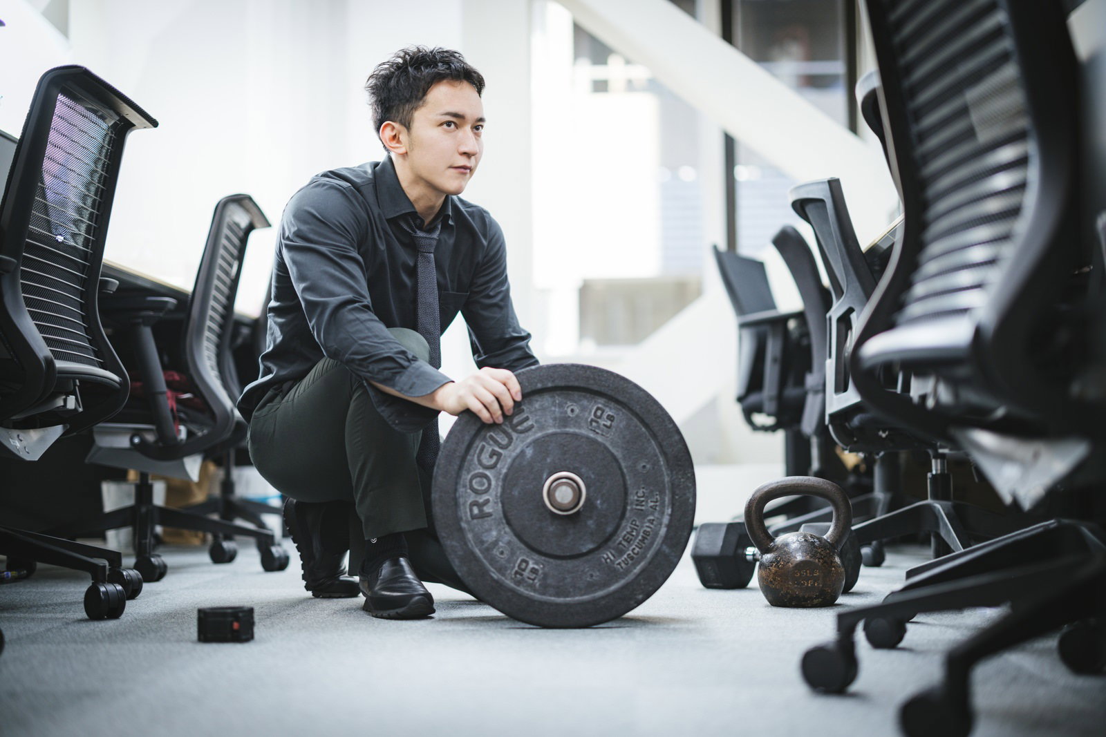 オフィスジムでバーベルを手にする営業服姿の男性経営者［モデル：鈴木秀］