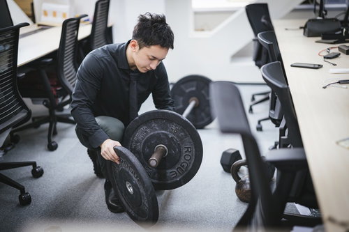 オフィスでバーベルの重りを調整する経営者